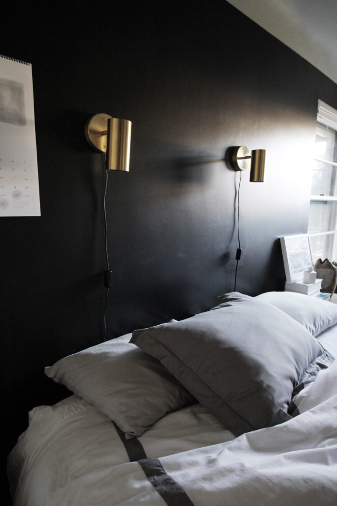 bedroom with dark walls, brass lights, gray bedspread