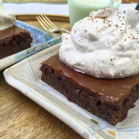 A close-up of a slice of chocolate cake topped with whipped cream, served on a decorative plate.