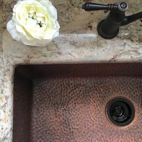 a copper kitchen sink with a flower on the countertop