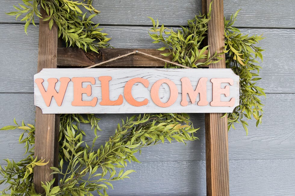 A crafting setup featuring a white wooden plaque with the word "WELCOME" in copper-colored letters, arranged on a white surface, ready to be assembled.