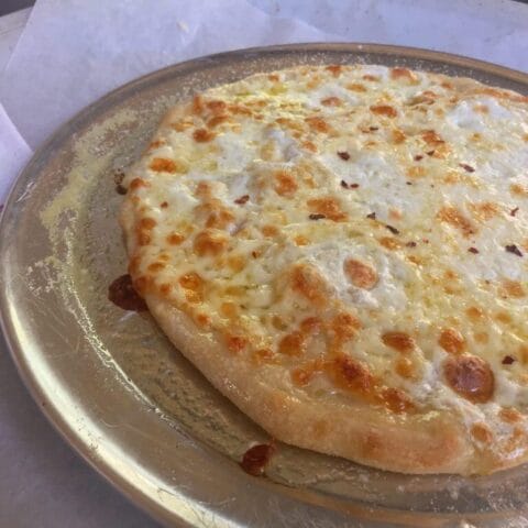 A freshly baked cheese pizza with a golden crust and melted cheese, topped with a sprinkle of red pepper flakes.