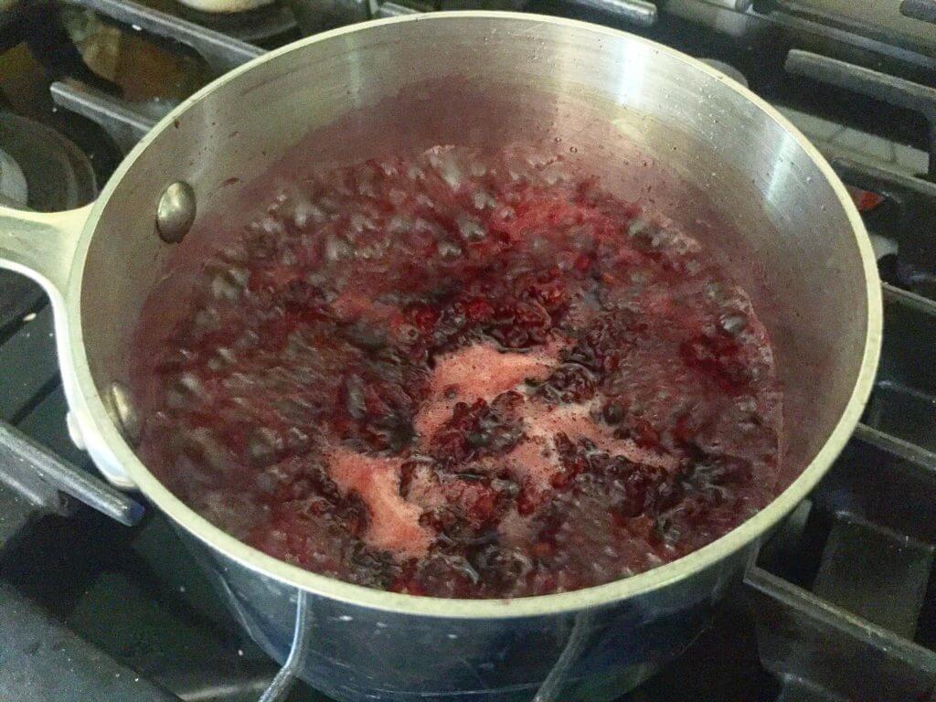 A pot of boiling blackberry mixture on a stove.