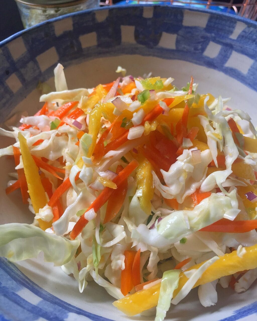 A bowl of fresh coleslaw made with shredded cabbage, carrots, bell peppers, onions, and mango, mixed together and ready to serve.