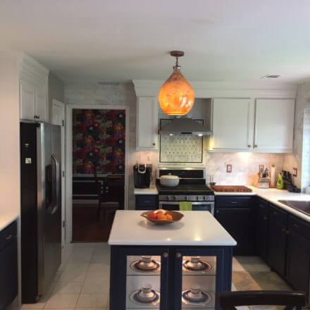 A modern kitchen with a central island, copper sink with a black gooseneck faucet and white countertops.