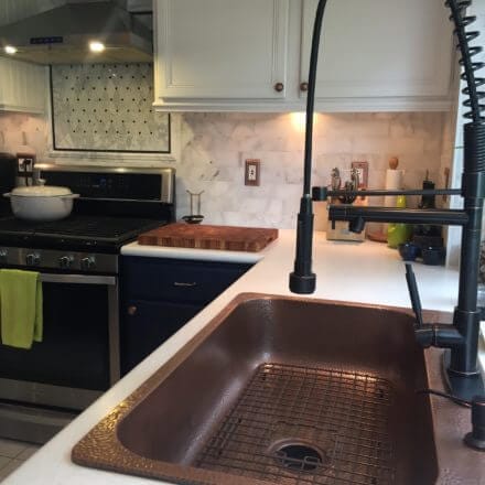 A drop-on copper kitchen sink with a black faucet.