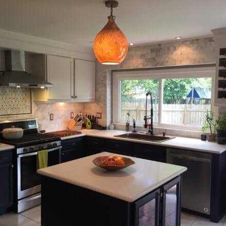 A modern kitchen with a central island, copper sink with a black gooseneck faucet and white countertops.