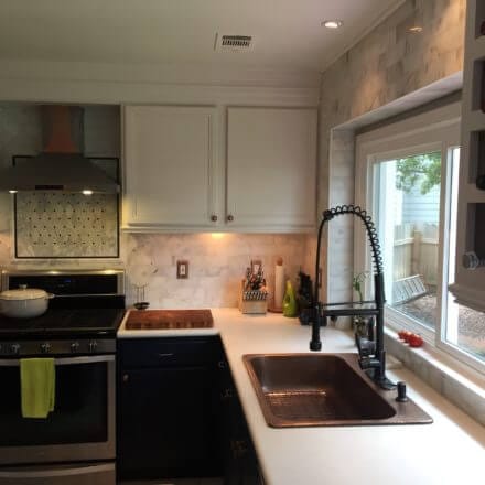 A modern kitchen with a central island, copper sink with a black gooseneck faucet and white countertops.