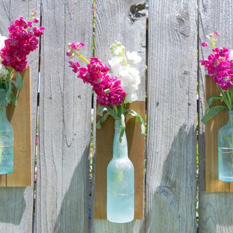 a diy bottle vase attached to a piece of wood by a copper wire