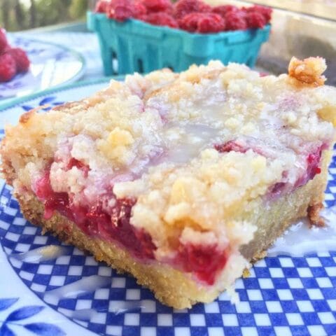 A slice of raspberry crumb bar with a crumbly top and visible raspberry filling, placed on a blue and white patterned plate.