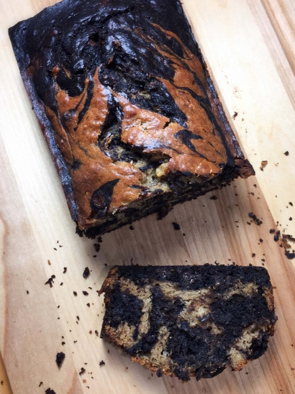 A loaf of marbled banana bread with one slice cut, showing the swirled pattern inside.