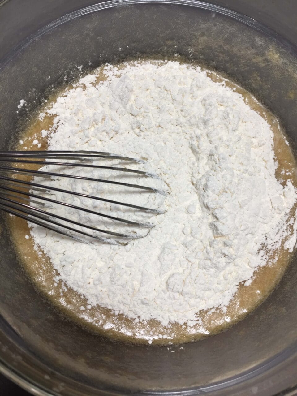 A mixing bowl with batter and flour being combined with a whisk.