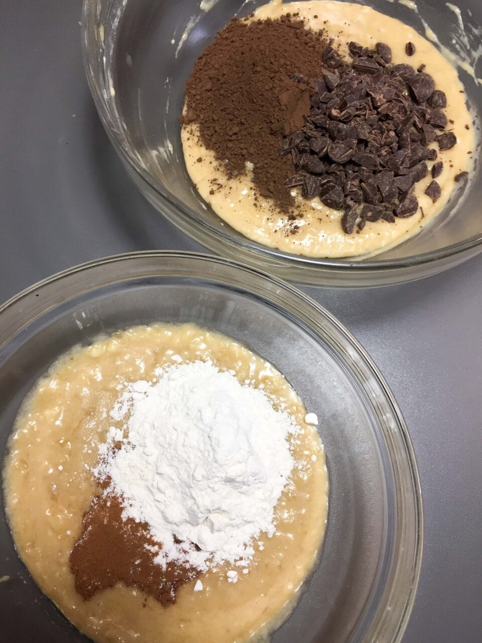 Two mixing bowls with batter: one with flour and cinnamon, the other with cocoa powder and chocolate chips.