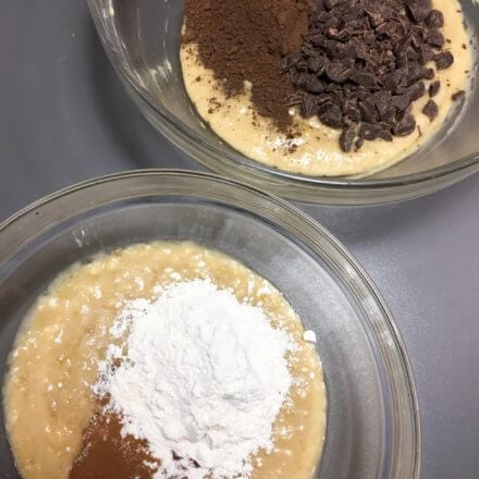Two mixing bowls with batter: one with flour and cinnamon, the other with cocoa powder and chocolate chips.