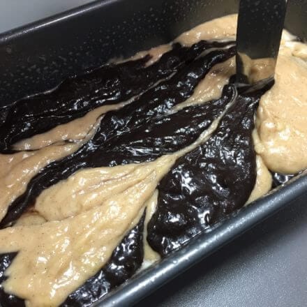 A loaf pan with swirled light and dark batter being mixed with a knife.