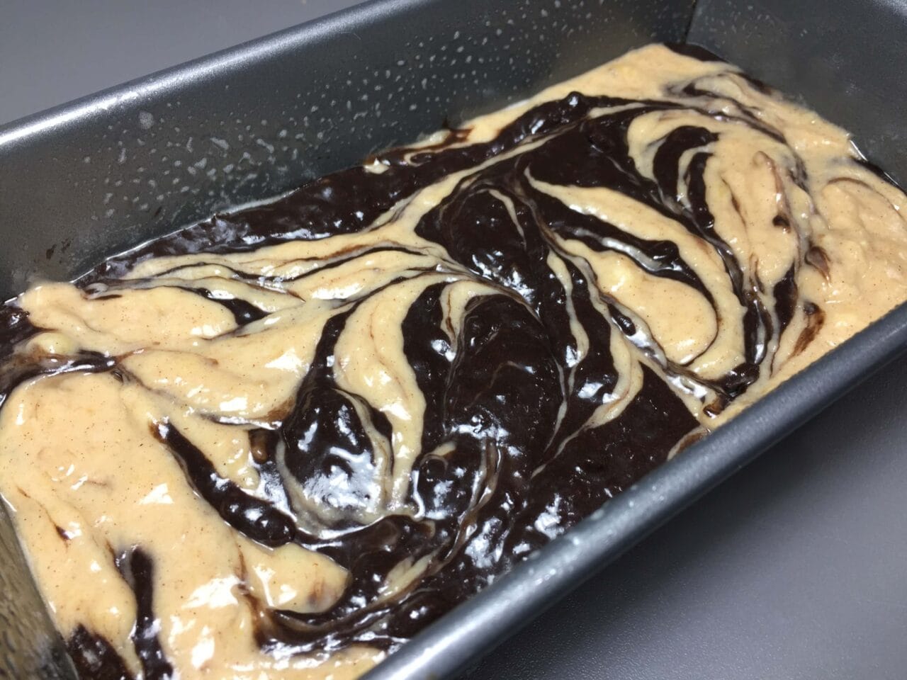 A loaf pan with marbled light and dark batter ready to be baked.