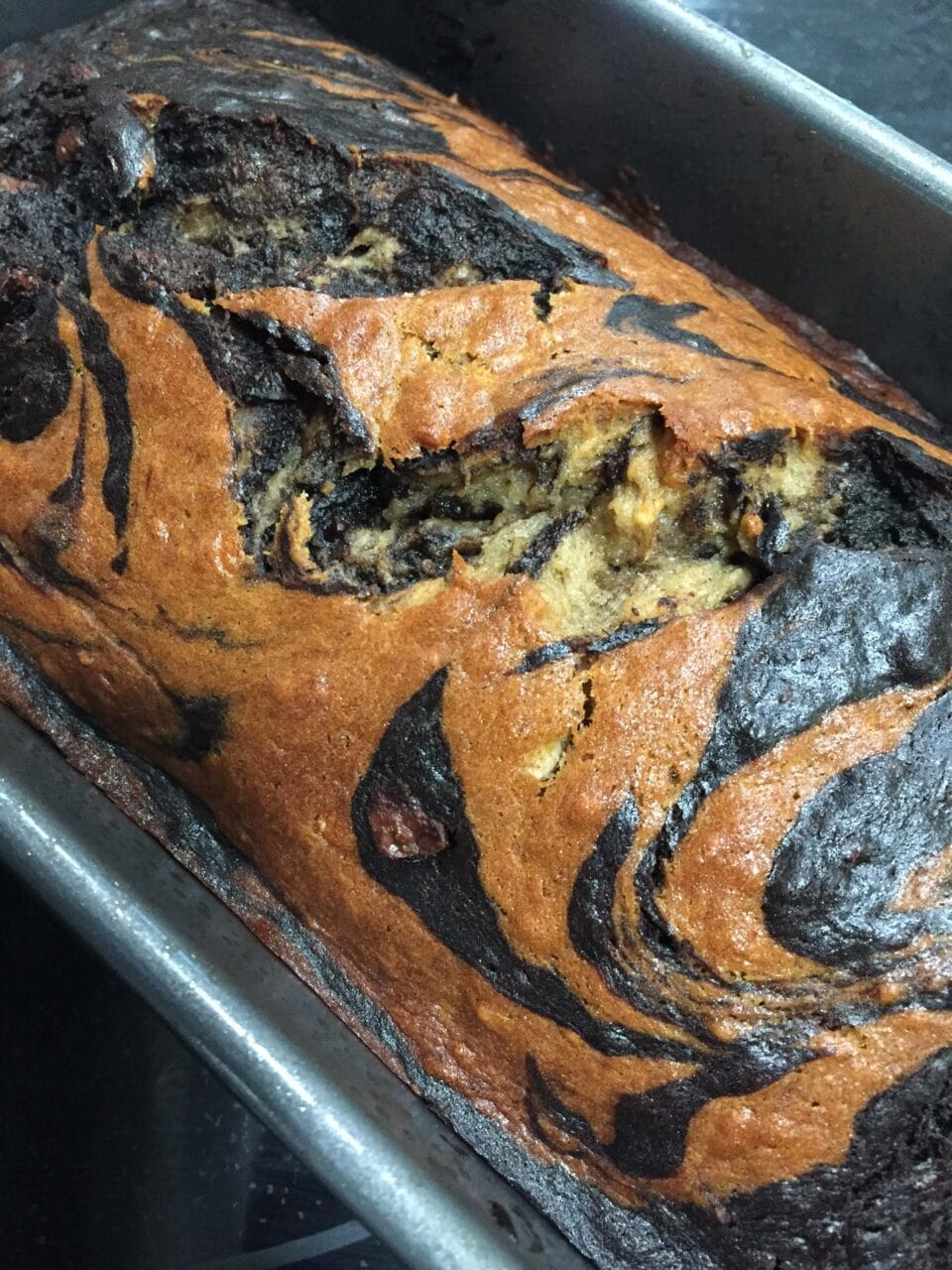 A baked loaf of marbled banana bread with swirls of light and dark batter in a loaf pan.