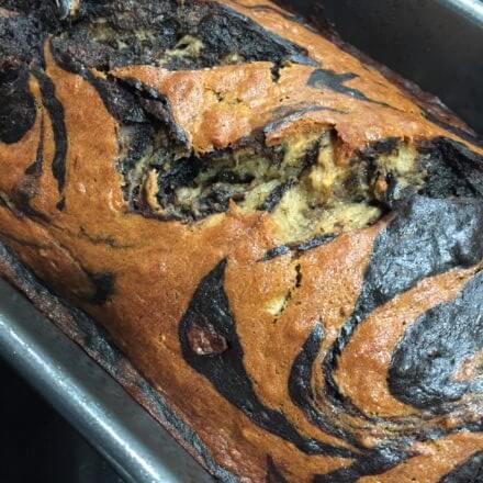A baked loaf of marbled banana bread with swirls of light and dark batter in a loaf pan.
