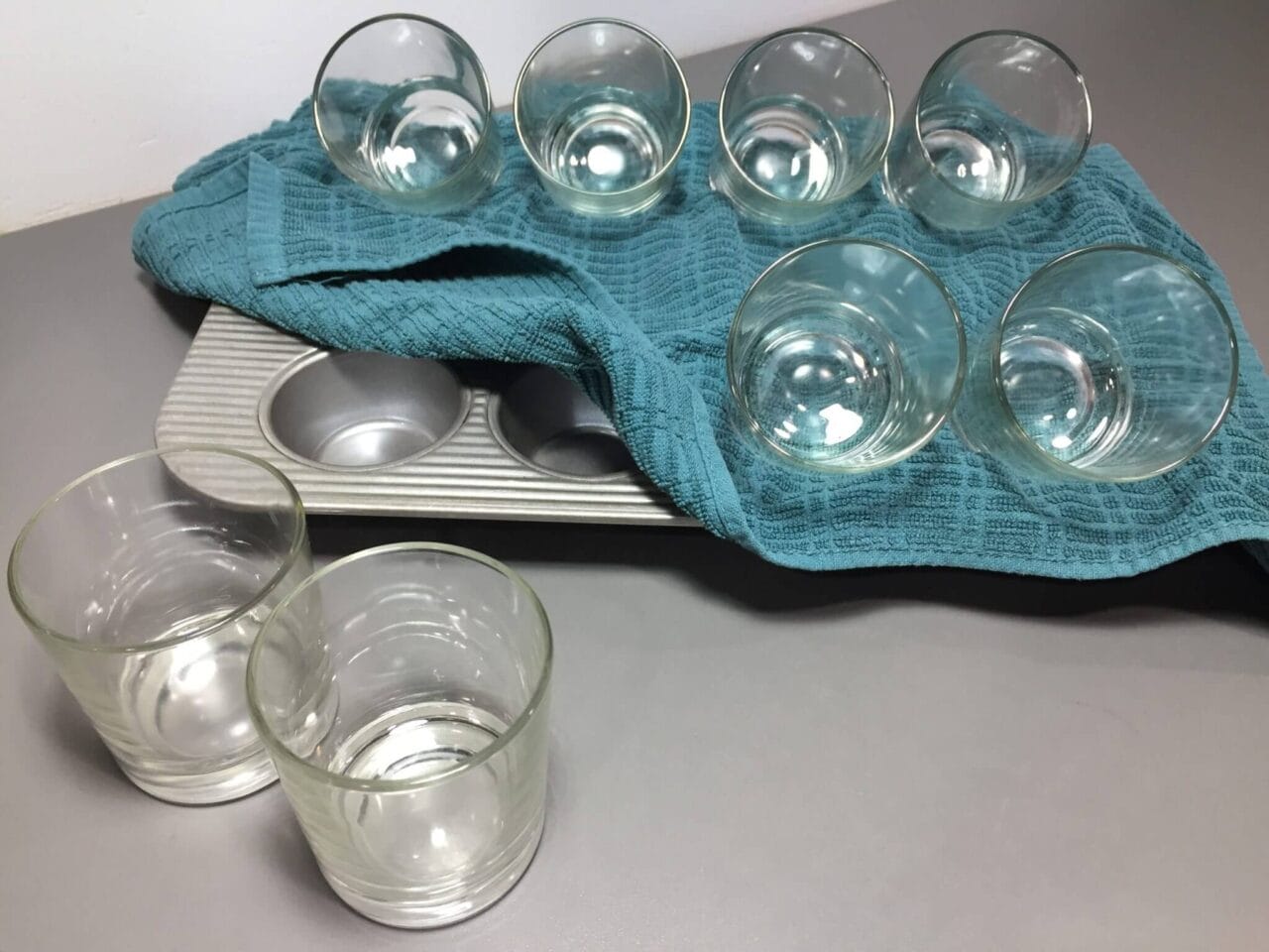 A baking tray with a blue cloth holding several upside-down glass cups, with two more glass cups standing upright on the side.