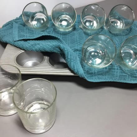 A baking tray with a blue cloth holding several upside-down glass cups, with two more glass cups standing upright on the side.