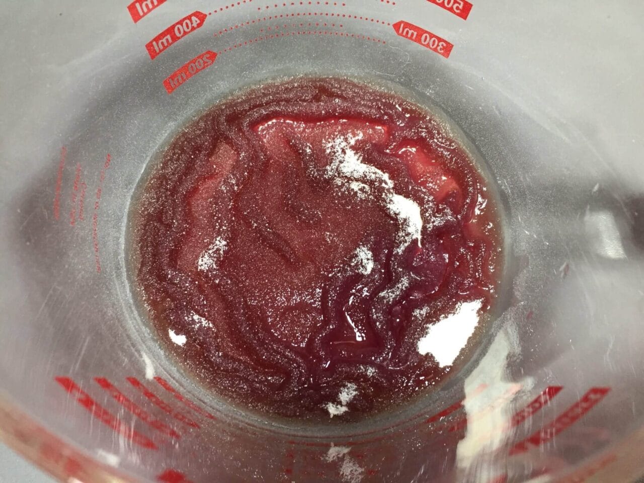 Top view of a measuring cup containing a red liquid with patches of white powder.