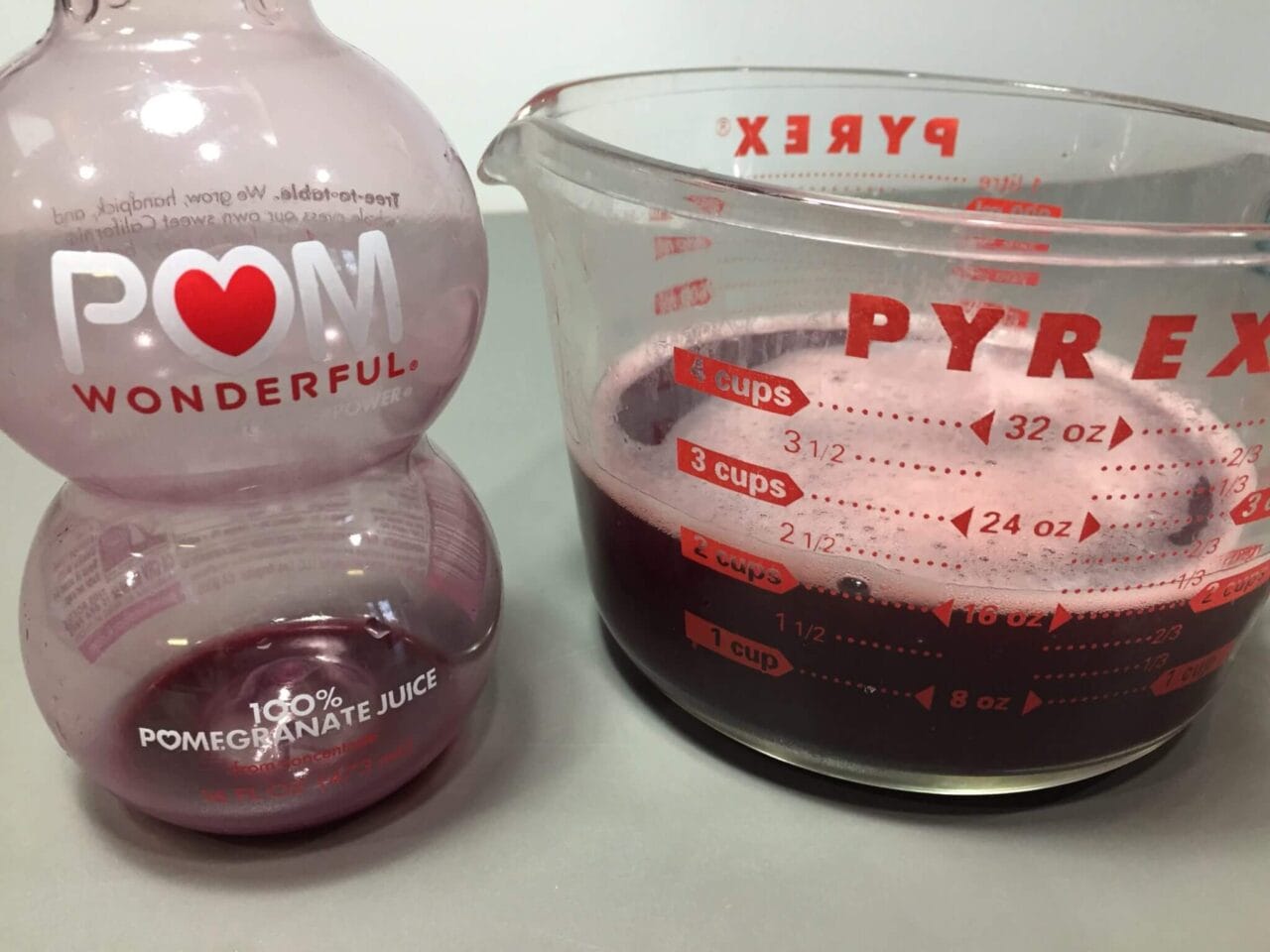 An empty POM Wonderful pomegranate juice bottle next to a Pyrex measuring cup filled with red liquid.