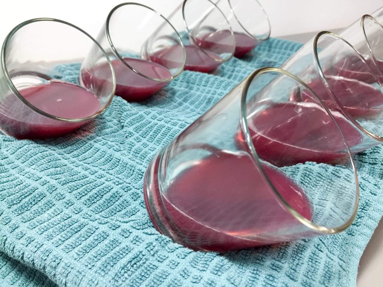 Several glass cups filled with red liquid placed on a blue cloth, all tilted at an angle.