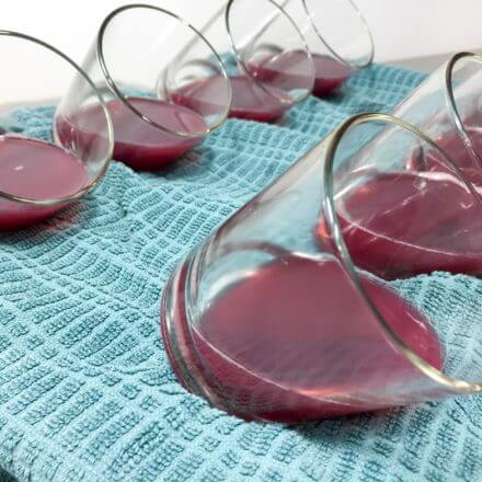 Several glass cups filled with red liquid placed on a blue cloth, all tilted at an angle.