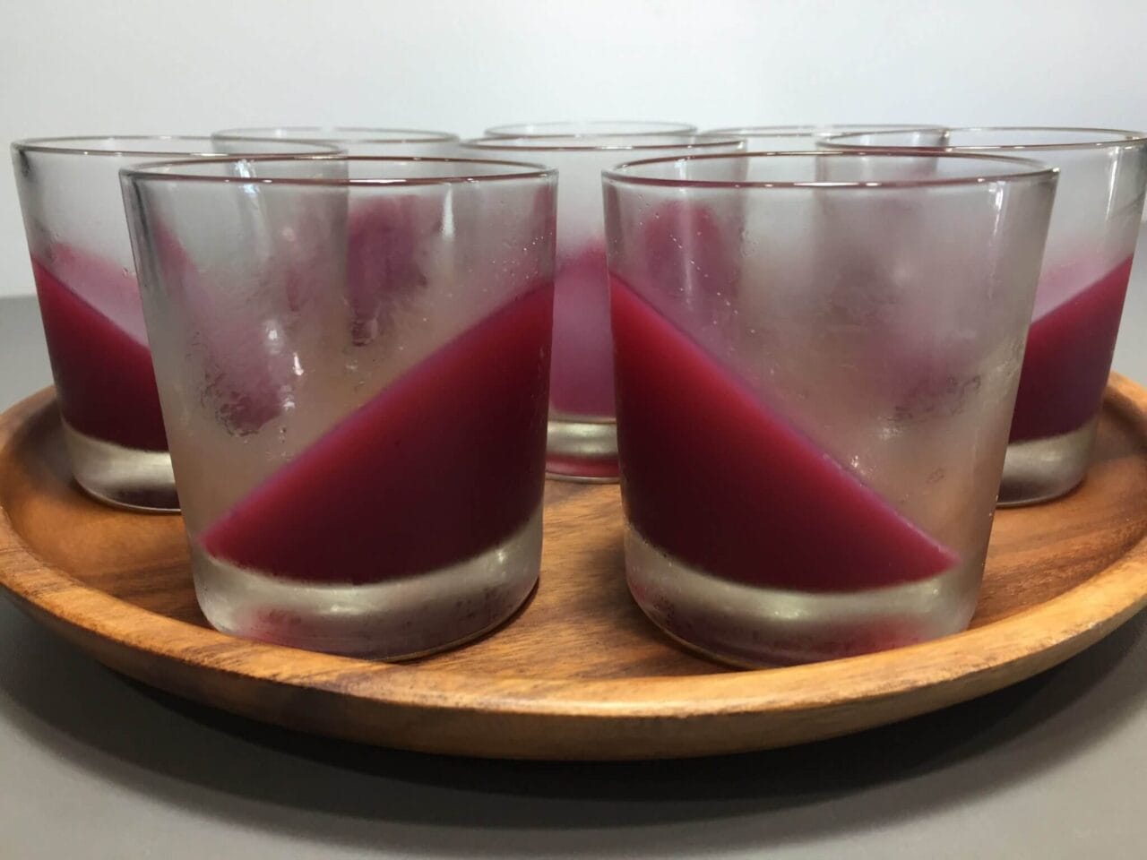 Several glass cups partially filled with red liquid, arranged on a wooden tray.