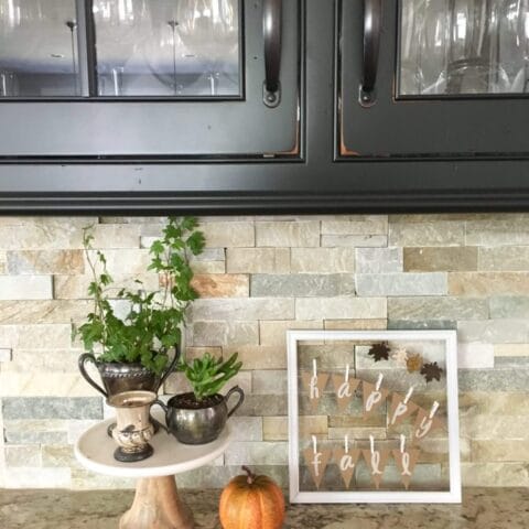 a fall decor frame on a kitchen countertop with a small pumpkin and vase