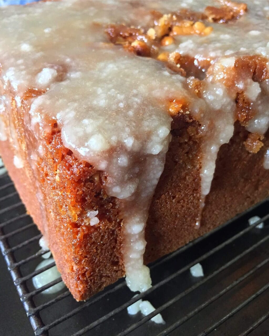 A glazed walnut cake on a cooling rack with glaze dripping down the sides.