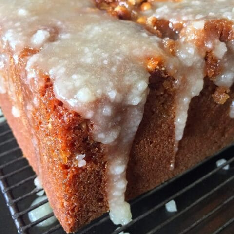 A glazed walnut cake on a cooling rack with glaze dripping down the sides.