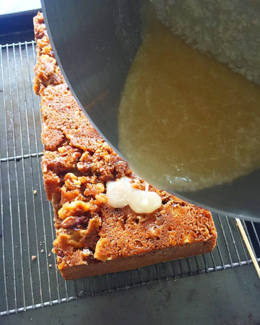 Pouring glaze over a nut-topped cake on a cooling rack.