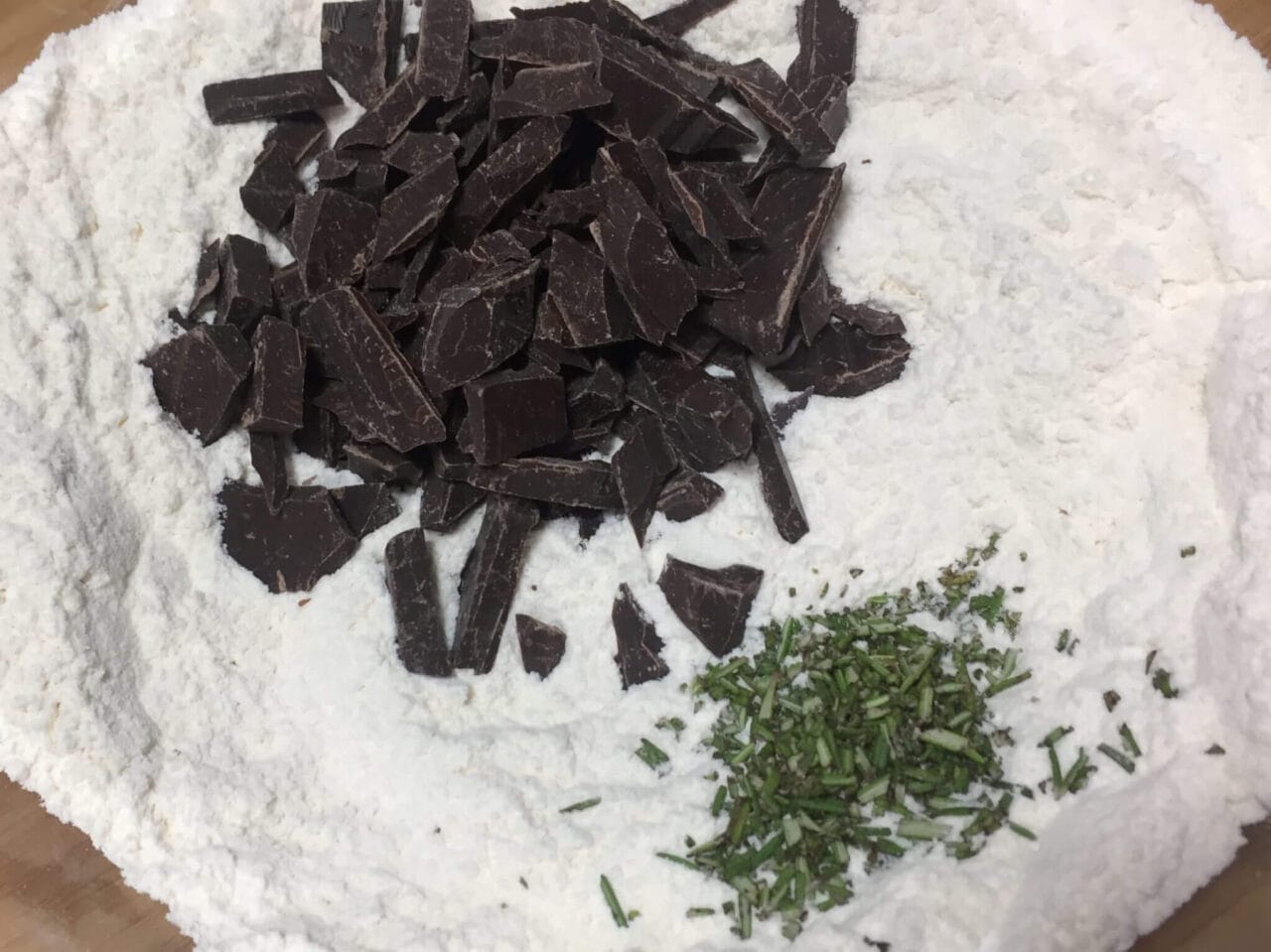 Chopped chocolate and finely chopped rosemary sit atop a bed of flour.