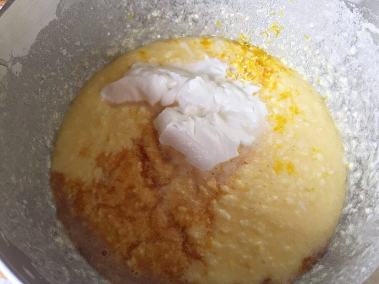 A mixing bowl with cake batter, lemon zest, and a dollop of sour cream.
