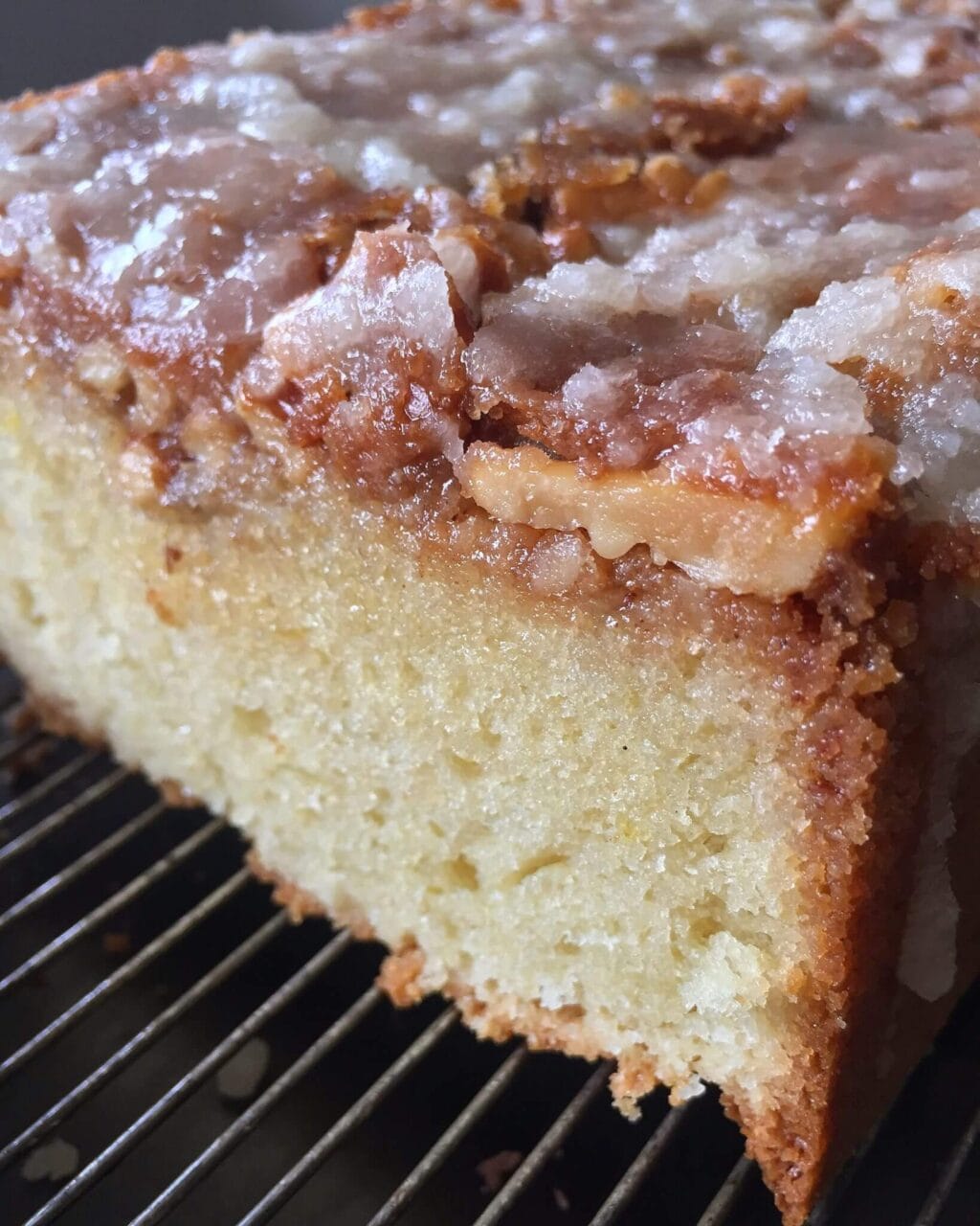 Close-up of a glazed walnut cake with a slice missing, resting on a cooling rack.
