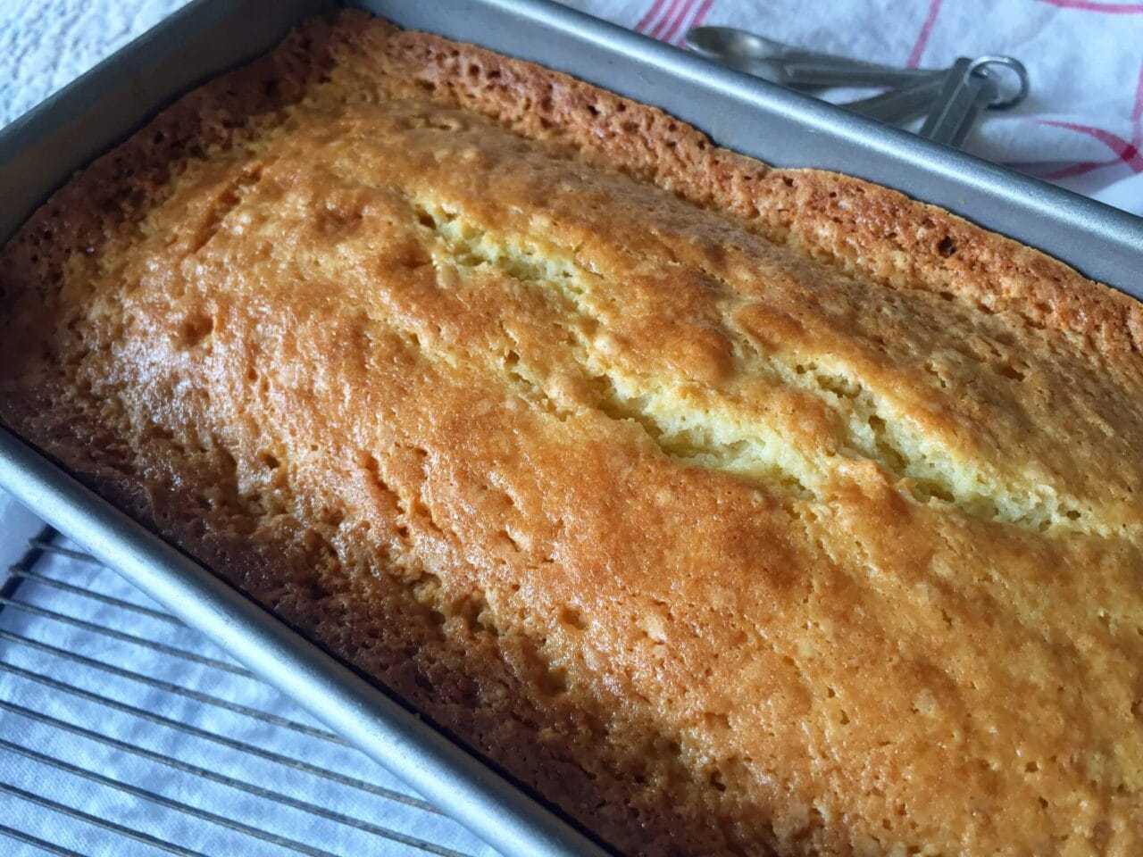A freshly baked loaf cake in a pan, cooling on a rack.