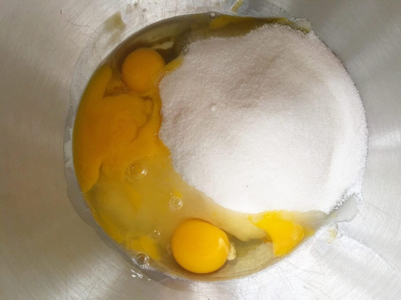 A mixing bowl containing eggs and sugar, ready to be mixed.