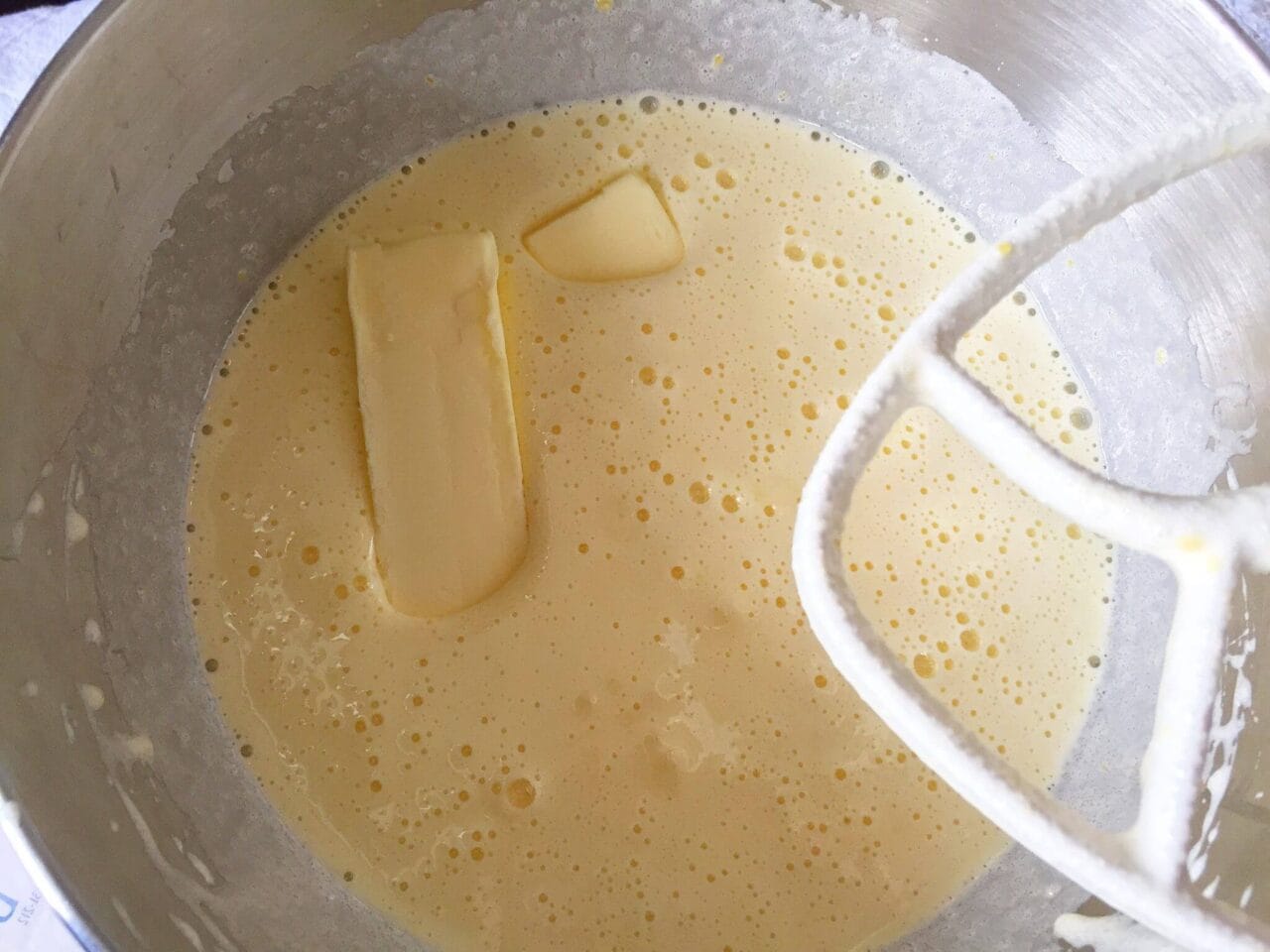A mixing bowl with cake batter and partially melted butter, next to a paddle attachment.