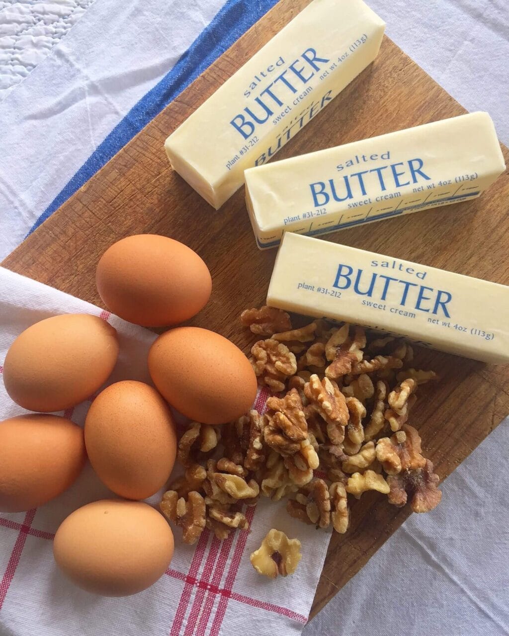 Sticks of butter, eggs, and walnuts arranged on a wooden cutting board.