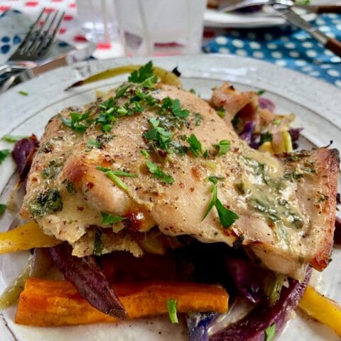 A plated serving of roasted honey mustard chicken with assorted root vegetables, garnished with fresh herbs.