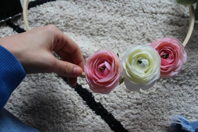 A hand holding three artificial flowers, two pink and one white, against a textured rug background.