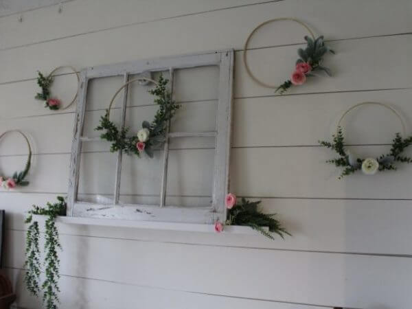 A vintage window frame mounted on a wall is surrounded by decorative hoops adorned with greenery and pink flowers.