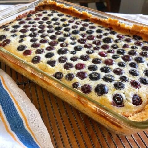 A freshly baked lemon blueberry dessert in a glass dish, cooling on a wire rack.