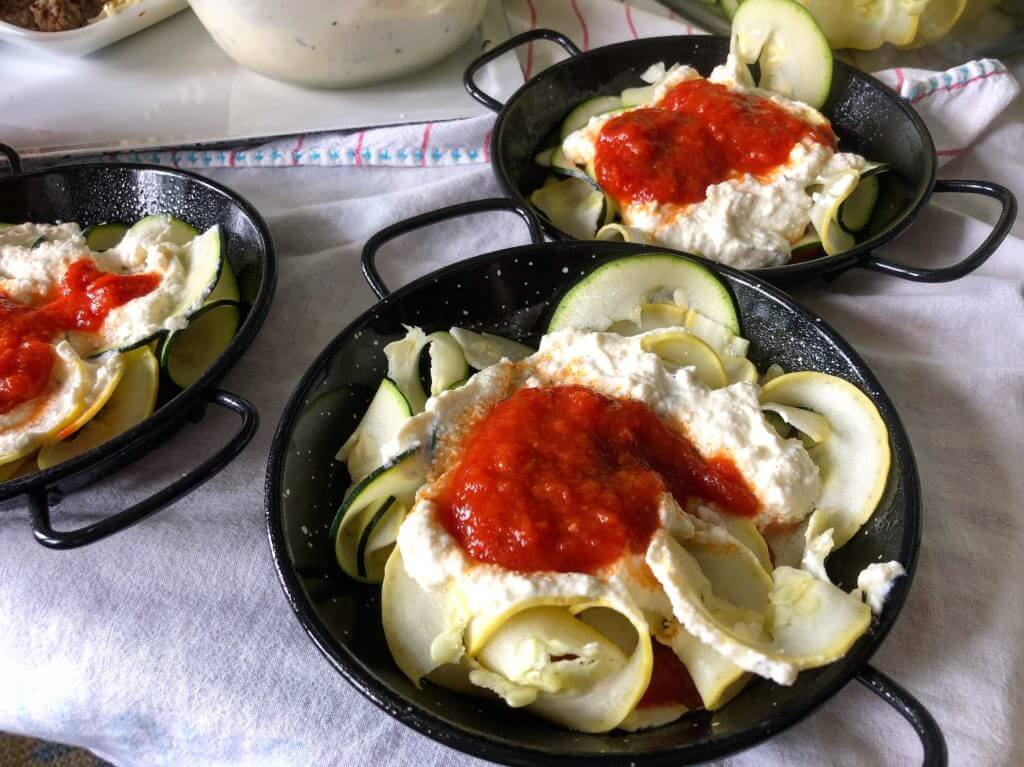Small black pans filled with sliced zucchini and yellow squash, topped with creamy dip and tomato sauce.