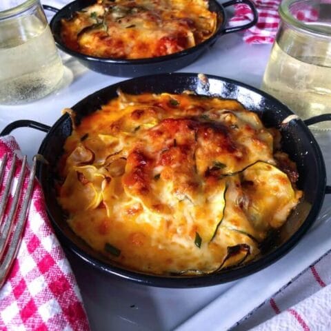 Baked zucchini and squash casserole topped with melted cheese in a small black pan, served with a glass of white wine.