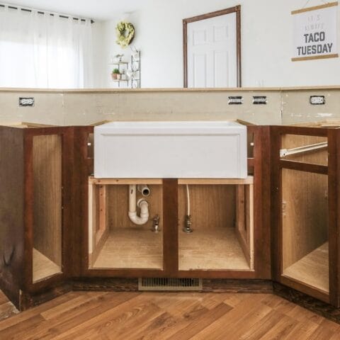 a white fireclay kitchen sink in a standard kitchen with cabinet doors off