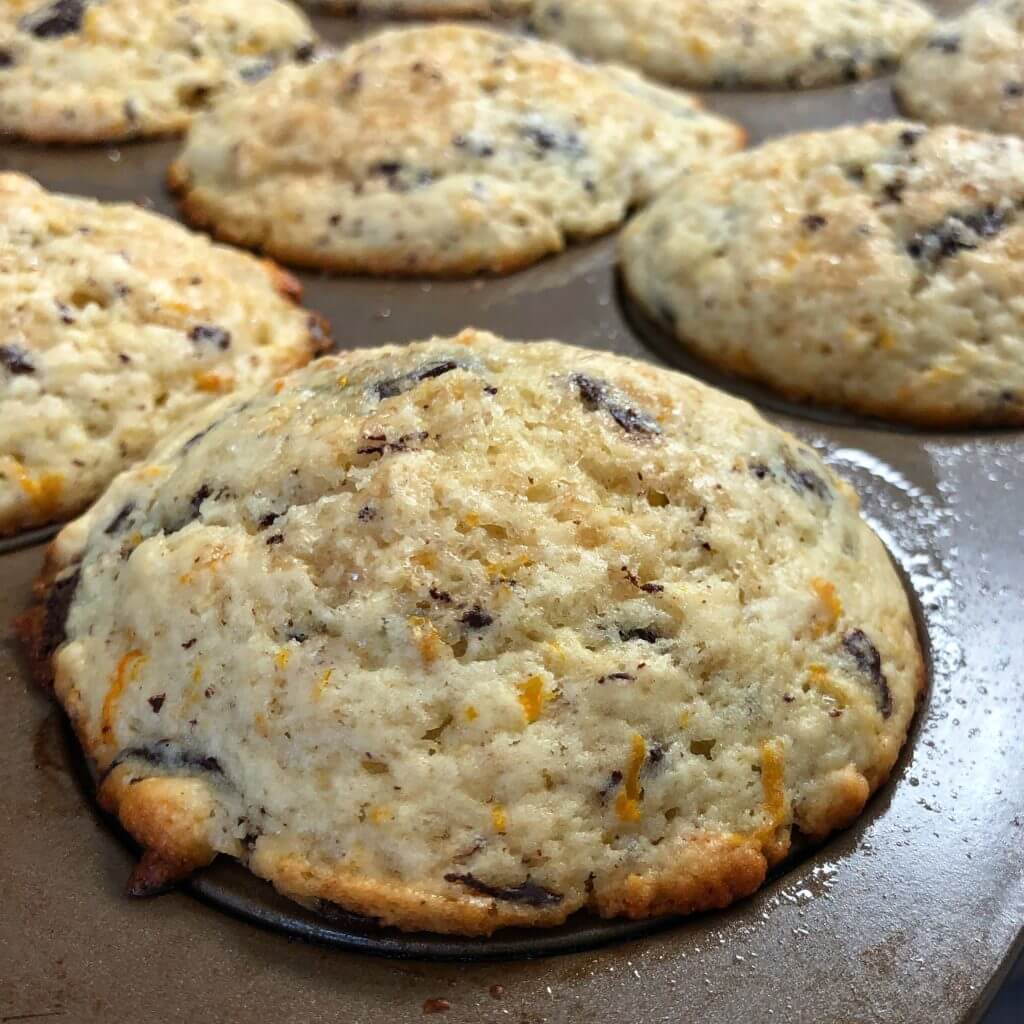 Freshly baked muffins with golden brown tops and visible chocolate chunks in a muffin tray.