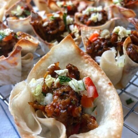 Close-up of crispy wonton cups filled with a mixture of ground meat, vegetables, and garnished with chopped cilantro and red bell peppers.