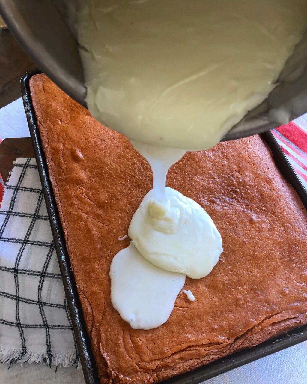 Pouring white frosting onto a freshly baked candy corn sheet cake.