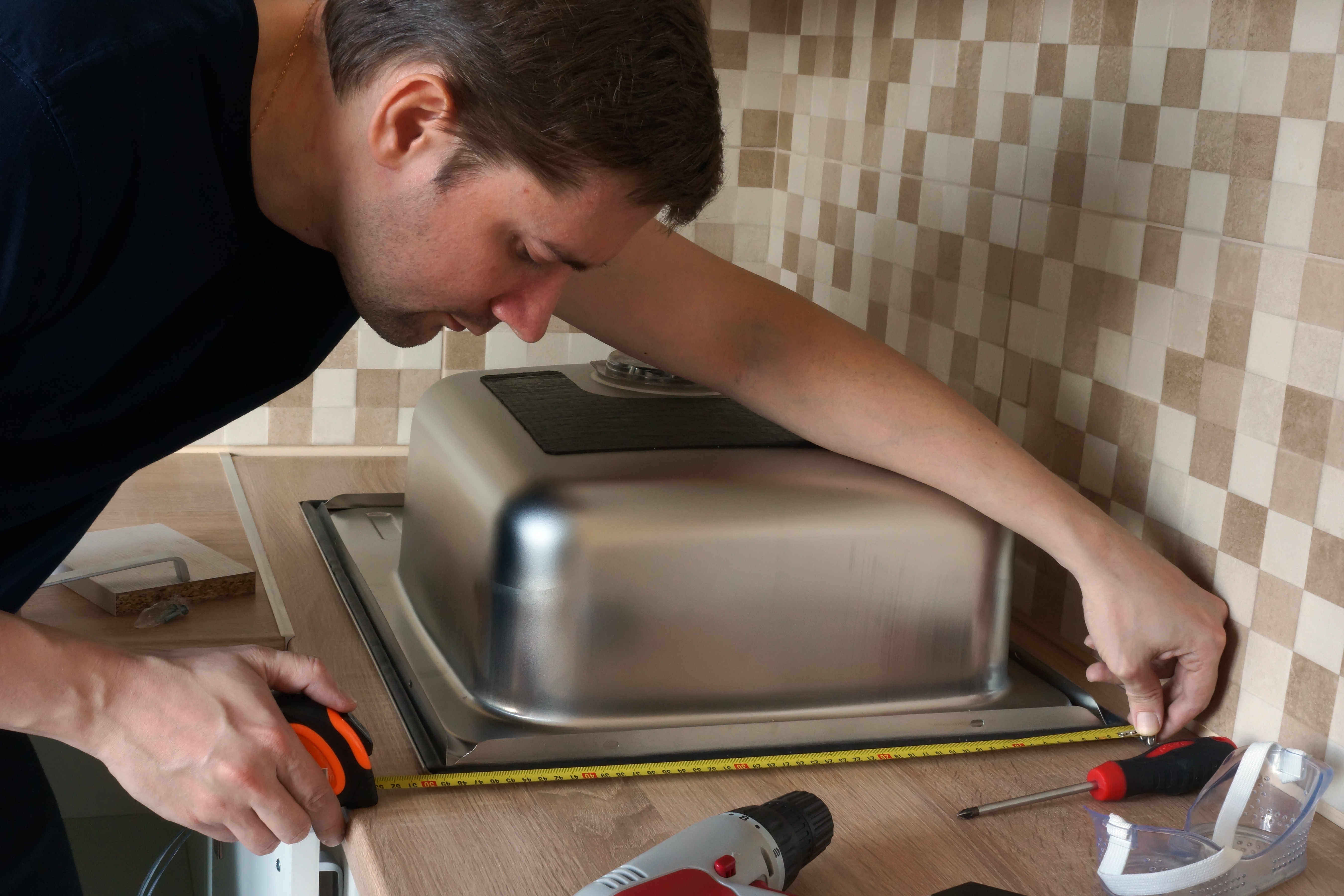 A person measuring a kitchen sink.